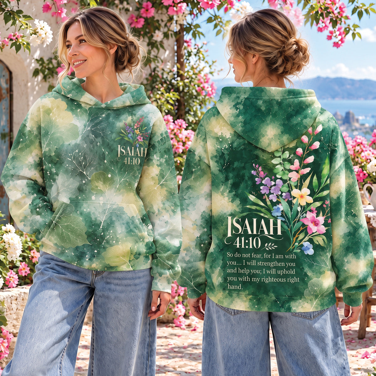 Two women modeling a green tie-dye hoodie with floral and Bible verse graphics, shown from the front and back in an outdoor garden setting.
