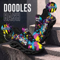 A pair of colorful graphic sneakers displayed on stone steps, with large text reading 'DOODLES BASH' and circular callouts showing custom name customization. The shoes have a black base with bright splatter-style graphics in pink, blue, yellow, and purple, plus white 'JESUS' and 'John 14:6' text.