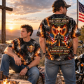 Two men wearing matching black graphic t-shirts with a fiery flame design and religious text, posed outdoors at sunset near a cross, American flag, and motorcycle.