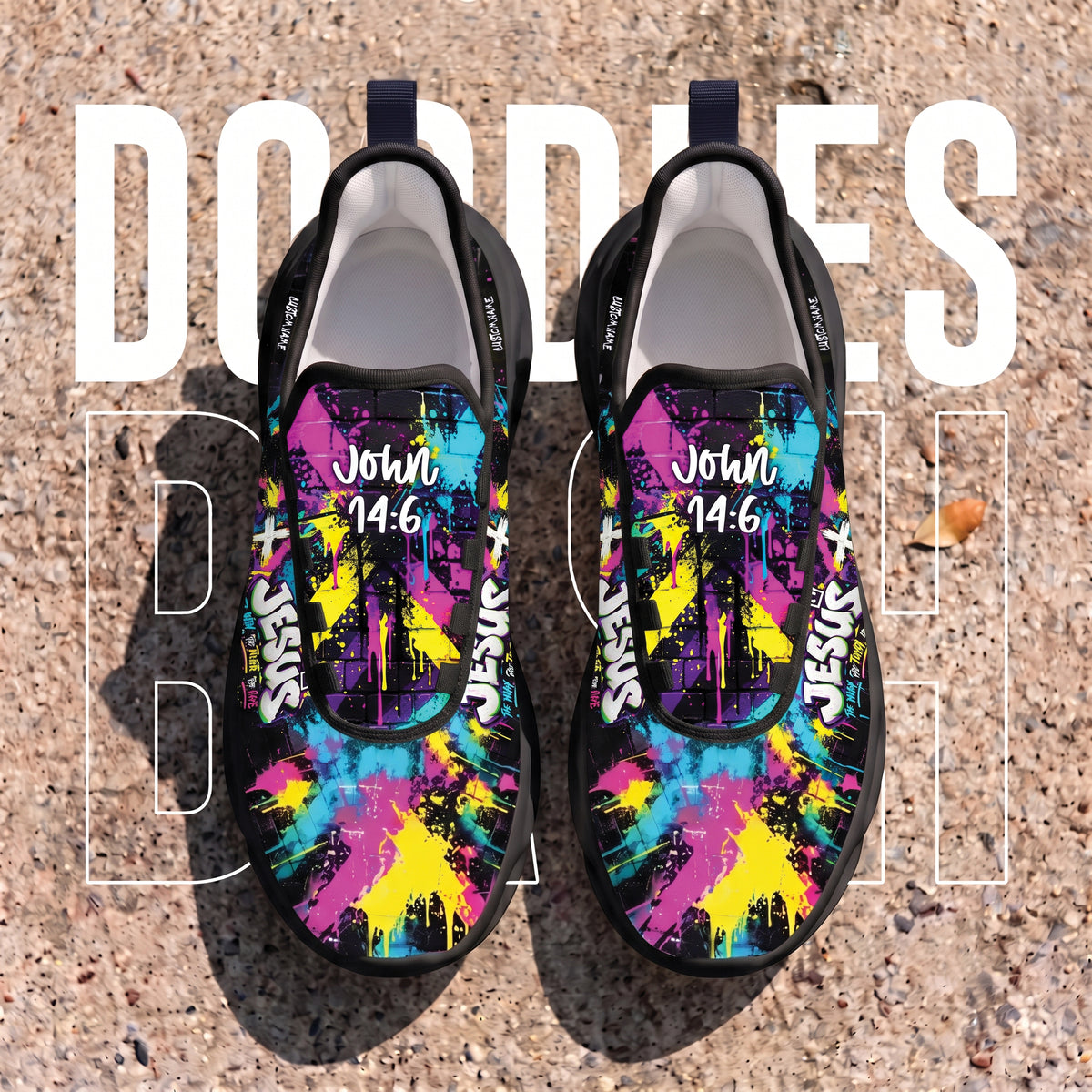A pair of slip-on sneakers placed on a textured concrete surface, featuring a colorful graffiti-style print with pink, blue, yellow, and black splashes, plus the text 'John 14:6' and 'Jesus' printed on the uppers.