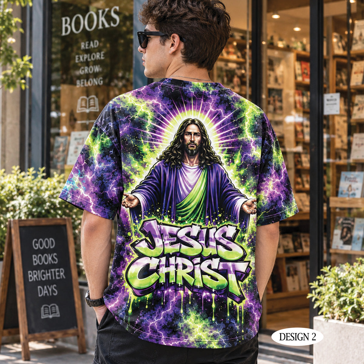 A man wearing a black t-shirt with a large, colorful graphic print of Jesus Christ with the text 'JESUS CHRIST' in green and purple graffiti-style lettering, shown from the back in front of a bookstore storefront.