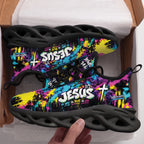 A pair of black athletic sneakers with a vibrant graffiti-style multicolor upper, held in a hand inside an open cardboard box. The shoes feature bold text including 'JESUS', 'John 14:6', and 'CUSTOM NAME' in white and yellow over a pink, blue, and yellow background.