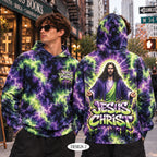 A man modeling a hoodie in an urban street setting, showing both front and back views of the garment. The hoodie features a purple and neon green lightning-bolt tie-dye pattern with a large graphic of Jesus Christ and the text 'JESUS CHRIST' on the back, and a smaller matching graphic on the front chest.